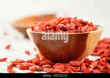 Baies de goji séchées dans un petit bol en bois, certains éparpillés sur des tableaux blancs sous la table Banque D'Images