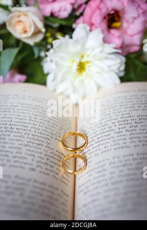 Bague de mariage sur un livre au milieu avec fond de bouquet Banque D'Images