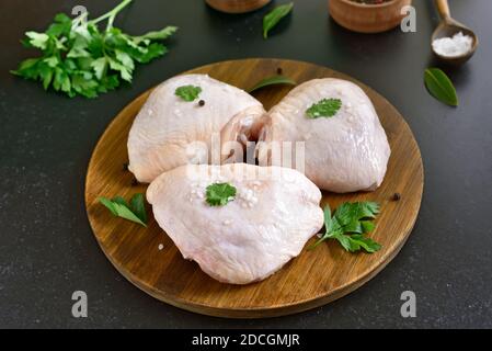 Cuisse de poulet crue sur planche à découper en bois sur fond sombre Banque D'Images