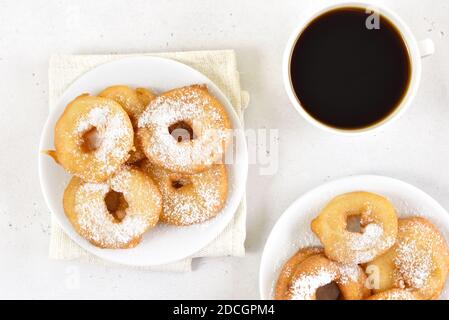 Beignets avec sucre en poudre sur plaque blanche, tasse de café noir sur fond de pierre clair. Vue de dessus, plan d'appartement Banque D'Images