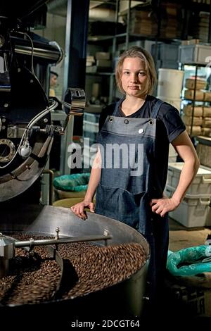 Le plat à rôtir pour jeunes femmes vérifie les grains de café lors de la torréfaction Banque D'Images