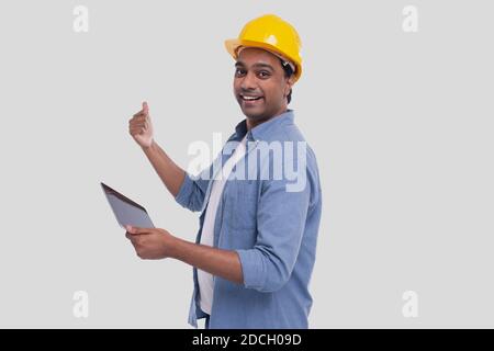 Travailleur de la construction tenant la tablette entre les mains montrant le dos. Homme utilisant la tablette. Tablette de maintien d'architecte. Casque dur jaune. Travailleur isolé Banque D'Images