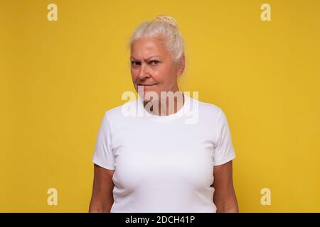 Femme âgée bouleversée perdue dans les pensées, manquer de vieux jours, penser ou réfléchir. Studio tourné sur un mur jaune. Banque D'Images