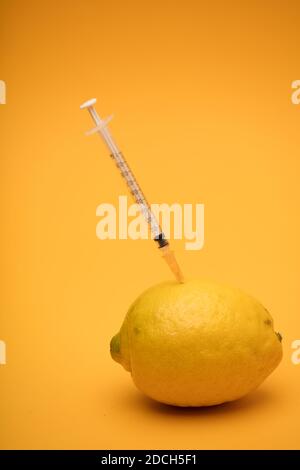 citron avec seringue bloquée, expérience de modification génétique, fond orange Banque D'Images