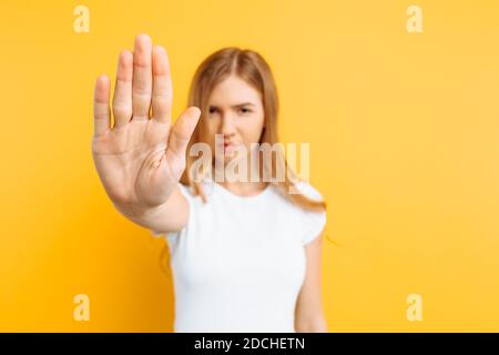 Une jeune fille sérieuse dans un T-shirt blanc montre une interdiction geste sur fond jaune Banque D'Images