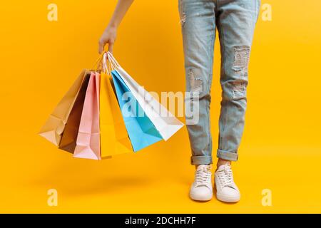 Gros plan des jambes, femme après le shopping stands avec beaucoup de sacs multicolores, sur fond jaune Banque D'Images