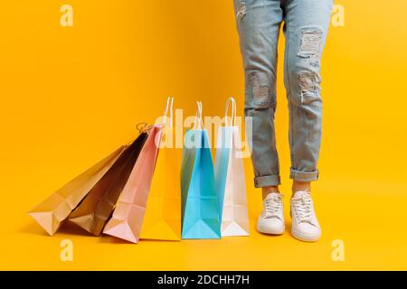 Gros plan des jambes, femme après le shopping stands avec beaucoup de sacs multicolores, sur fond jaune Banque D'Images