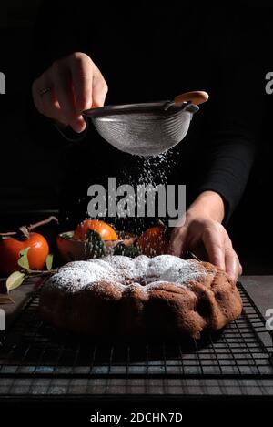 La main de femme saupoudrer le sucre glace sur un gâteau de bundt frais. Arrière-plan sombre. Banque D'Images
