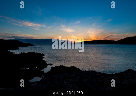 Le soleil se couche derrière le promontoire de Creag a' Mhàil à la baie de Scourie, sur la côte nord-ouest de l'Écosse. Juin. Banque D'Images