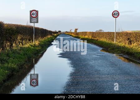 Panneau de limite de vitesse de 40 km/h sur la route de campagne nommée comme une route tranquille avec réflexion dans la flaque, East Lothian, Écosse, Royaume-Uni Banque D'Images
