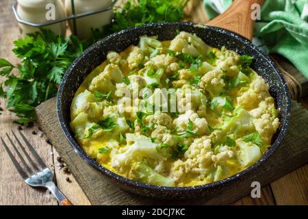 Un petit déjeuner diététique ou un déjeuner sain. Omelette aux oeufs avec chou-fleur dans une poêle en fonte sur une table rustique en bois. Banque D'Images