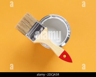 Nouvelle brosse en soie naturelle avec manche en bois sur le bord d'une peinture blanche ouverte peut sur fond texturé jaune vif. Travaux de peinture de construction Banque D'Images