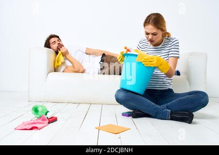 Le mari repose sur le canapé pendant que sa femme nettoie vers le haut de la décoration intérieure Banque D'Images