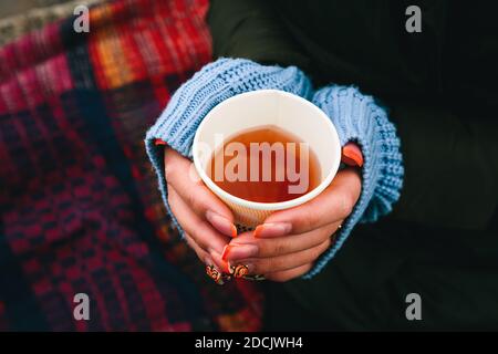 Une femme européenne tenant une tasse de thé dans les mains froides sur fond de plaid. Chauffer les mains avec du thé chaud et des manches de chandail. Banque D'Images