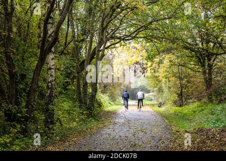 Deux cyclistes traversent les feuilles mortes à côté d'arbres affichant des couleurs d'automne sur le chemin de fer de Bristol et Bath. Banque D'Images