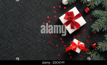 Boîtes-cadeaux de Noël élégantes avec noeuds en ruban rouge, branches en sapin, confetti étincelants sur fond noir. Banderole de Noël, carte de vœux du nouvel an Banque D'Images