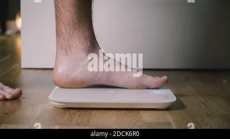 Homme marche sur des balances numériques en verre pour vérifier le poids. Poids masculin sur les pèse-personne dans les chambres domestiques, vue rapprochée des pieds. Pieds d'homme sur balance électronique Banque D'Images