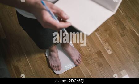 Homme marche sur des balances numériques en verre pour vérifier le poids. Poids masculin sur les pèse-personne dans les chambres domestiques, vue rapprochée des pieds. Pieds d'homme sur balance électronique Banque D'Images