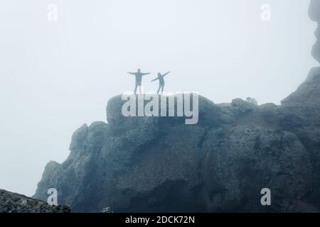 Couple heureux à bras ouverts célébrant après l'escalade de la montagne rocheuse dans le parc naturel de Roque Nublo, Gran Canaria. Silhouette de randonneurs sur la falaise Banque D'Images