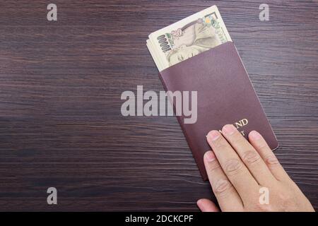 Main de l'homme tenant un passeport international et de l'argent japonais sur une table marron en bois foncé. Banque D'Images