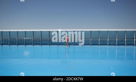 une femme marche seule sur le pont d'un navire à l'intérieur une robe rouge Banque D'Images