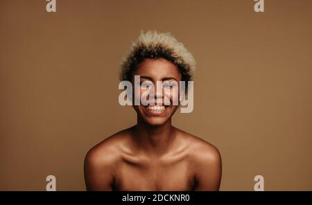 Gros plan sur une femme afro-américaine en train de rire. Femme aux cheveux bouclés courts sur fond marron. Banque D'Images