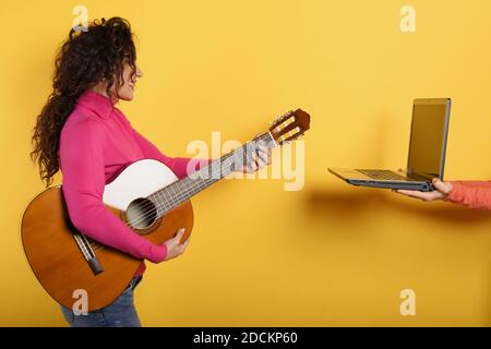 Happy Woman suit une leçon de guitare en ligne. Arrière-plan jaune Banque D'Images