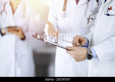 Des médecins inconnus, deux hommes et une femme, discutent des examens médicaux, tout en se tenant au bureau ensoleillé de l'hôpital. Médecins utilisant des planches à découper pour le remplissage Banque D'Images