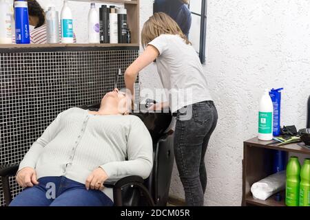 Femme coiffeur lave la tête de la femme cliente avant de couper dans un évier spécial dans le salon de coiffure dans la vraie journée de travail. Banque D'Images