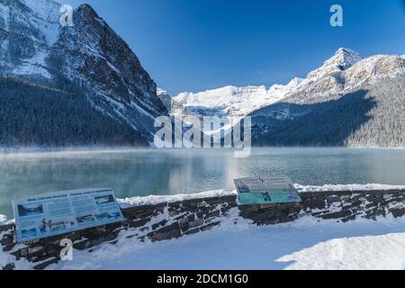 Lac Louise en début d'hiver, jour ensoleillé le matin. Brume flottant sur la surface turquoise de l'eau. Ciel bleu clair, montagnes enneigées en arrière-plan. Banque D'Images