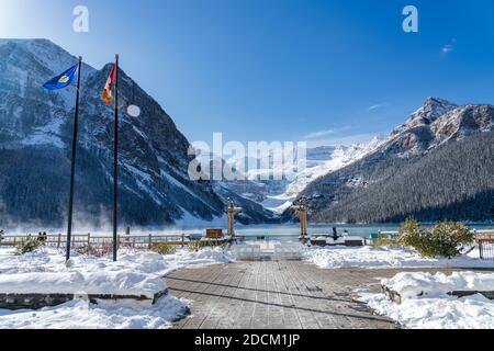 Fairmont Chateau Lake Louise en début d'hiver, jour ensoleillé le matin. Brume flottant sur la surface turquoise de l'eau. Ciel bleu clair, montagnes enneigées Banque D'Images