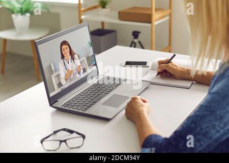 Femme mature prenant des notes tout en écoutant un médecin en ligne donner des conseils de santé Banque D'Images