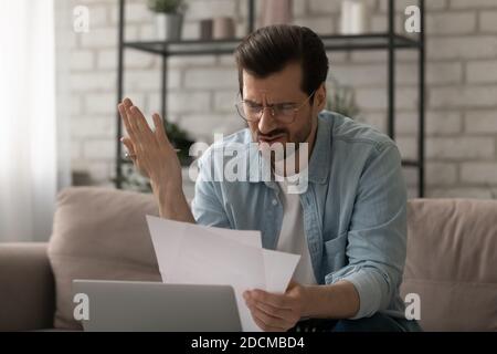 Jeune homme frustré dans les verres regardant le papier, se sentant stressé. Banque D'Images