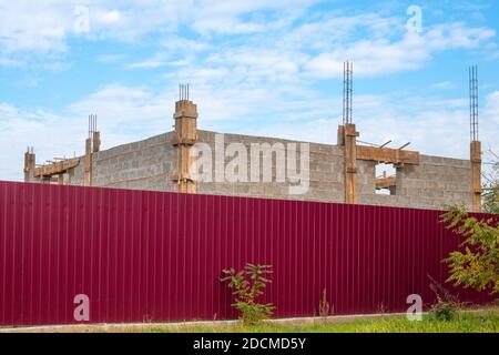 Étapes de construction. Maison de bloc de cinder avec raccords saillants derrière une clôture bordeaux. Banque D'Images