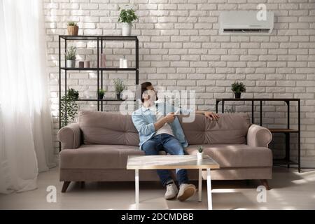 Jeune homme détendu qui active le système de climatisation à la maison. Banque D'Images