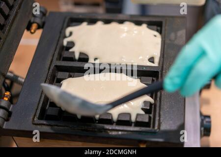 Fer à repasser dans la cuisine. Préparer des gaufres faites maison, verser une pâte. Préparation de gaufres faites maison dans la machine à gaufres double. Mise au point sélective Banque D'Images