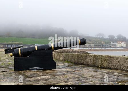 Canons sur l'est Breakwater de Lyme Regis Harbour à Dorset avec le bas nuage et le brouillard obscurcissant partiellement Langmoor et les jardins de Lister. Banque D'Images