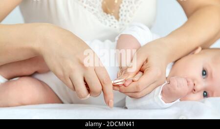 La mère coupe les ongles de bébé sur fond clair. Concentration sélective. Personnes. Banque D'Images