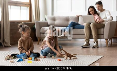 Couple de repos sur le canapé avec ordinateur portable tandis que les filles jouent des jouets Banque D'Images