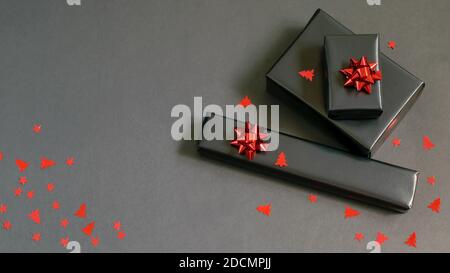 Boîtes-cadeaux de Noël faites à la main enveloppées de papier noir, de rubans rouges étincelants et de confettis festifs. Kit d'entretien, cadeaux faits main, concepts de bricolage. Banque D'Images