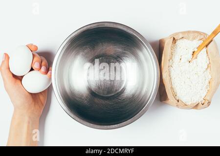 Composition de cuisson à plat, femelle tenant les oeufs à la main à côté du bol vide et paquet de farine sur fond blanc. Banque D'Images