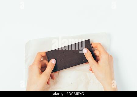 Flat Lay les mains des femmes tenant toute la barre de chocolat noir biologique sur la table blanche. Banque D'Images