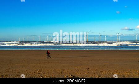 Un couple marchant sur la plage de Redcar avec le soleil éclairé Teesside Parc éolien offshore derrière Banque D'Images