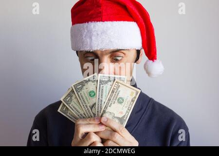 Jeune homme avec chapeau de père Noël regardant des billets de dollar avec des yeux incrédules sur fond blanc. Personne avec un regard intense et de l'argent dans les mains Banque D'Images