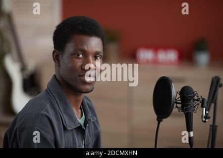 Portrait d'un jeune musicien afro-américain regardant la caméra tout en étant assis au microphone dans un studio d'enregistrement à domicile, espace de copie Banque D'Images