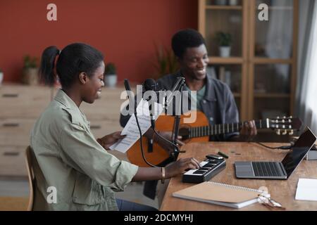 Vue latérale sur un jeune couple afro-américain qui compose de la musique dans un studio d'enregistrement à domicile, espace de copie Banque D'Images