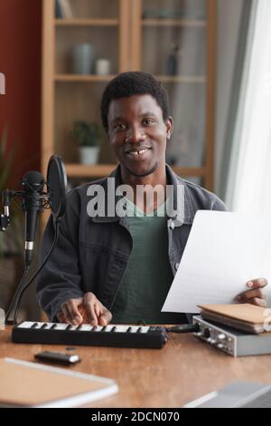 Portrait vertical d'un homme afro-américain souriant chantant au micro pendant que enregistrement de musique dans un studio personnel Banque D'Images