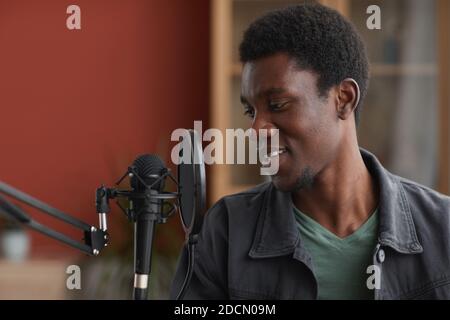 Portrait en vue latérale d'un jeune homme afro-américain chantant au micro tout en enregistrant de la musique dans un studio à domicile, dans un espace de copie Banque D'Images