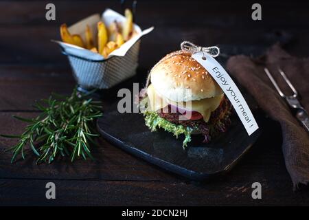 Hamburgers au fromage végétarien faits maison et frites dans une obscurité panneau en bois sur une table en bois brun foncé à côté Une serviette de table en lin brun avec un signe de plaisir Banque D'Images