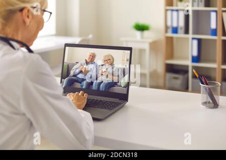 Médecin assis à une table devant un ordinateur portable et parlant à un couple âgé par liaison vidéo. Banque D'Images